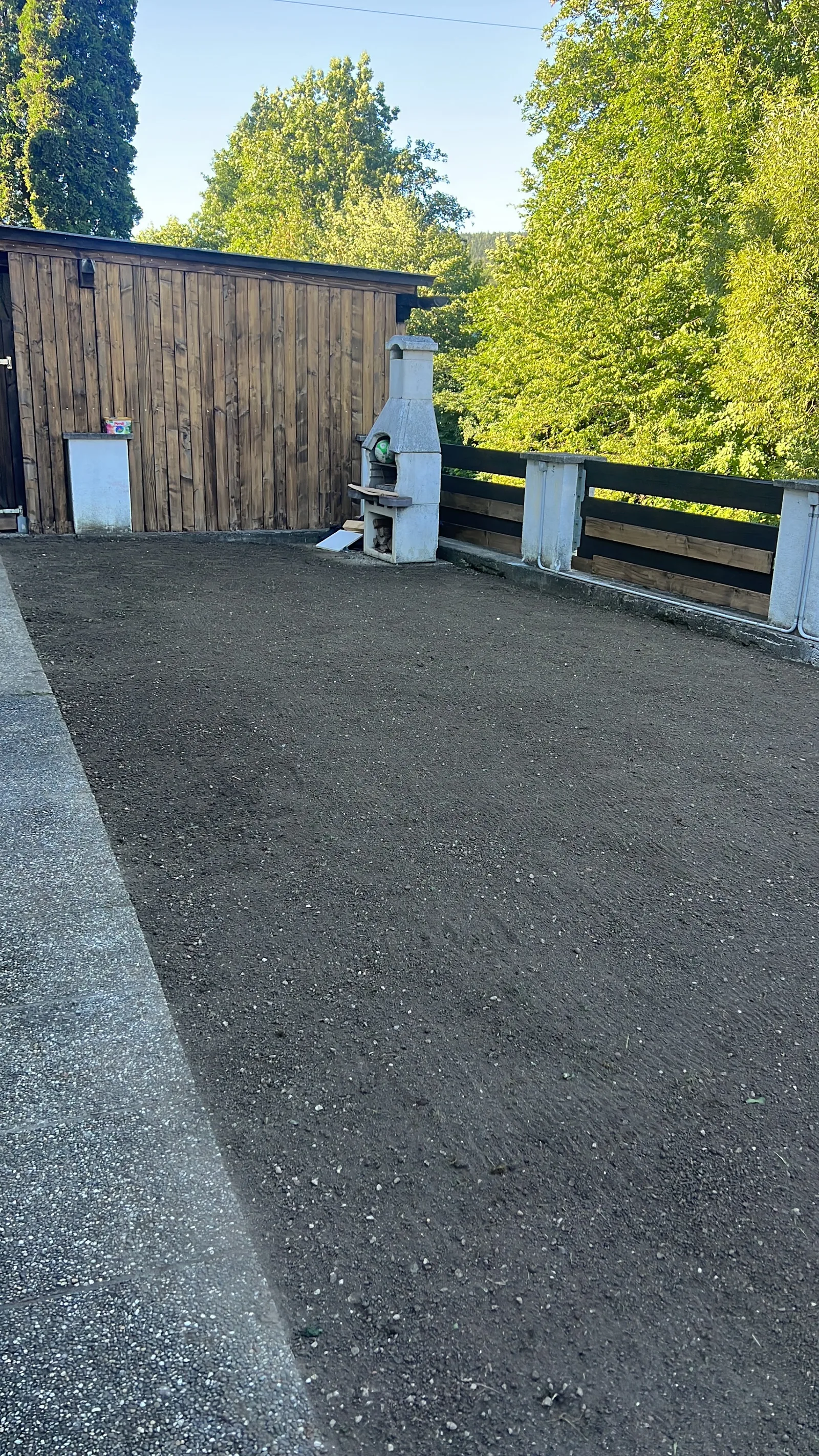 Planierte Gartenfläche neben einem Holzgebäude und einem Grillkamin