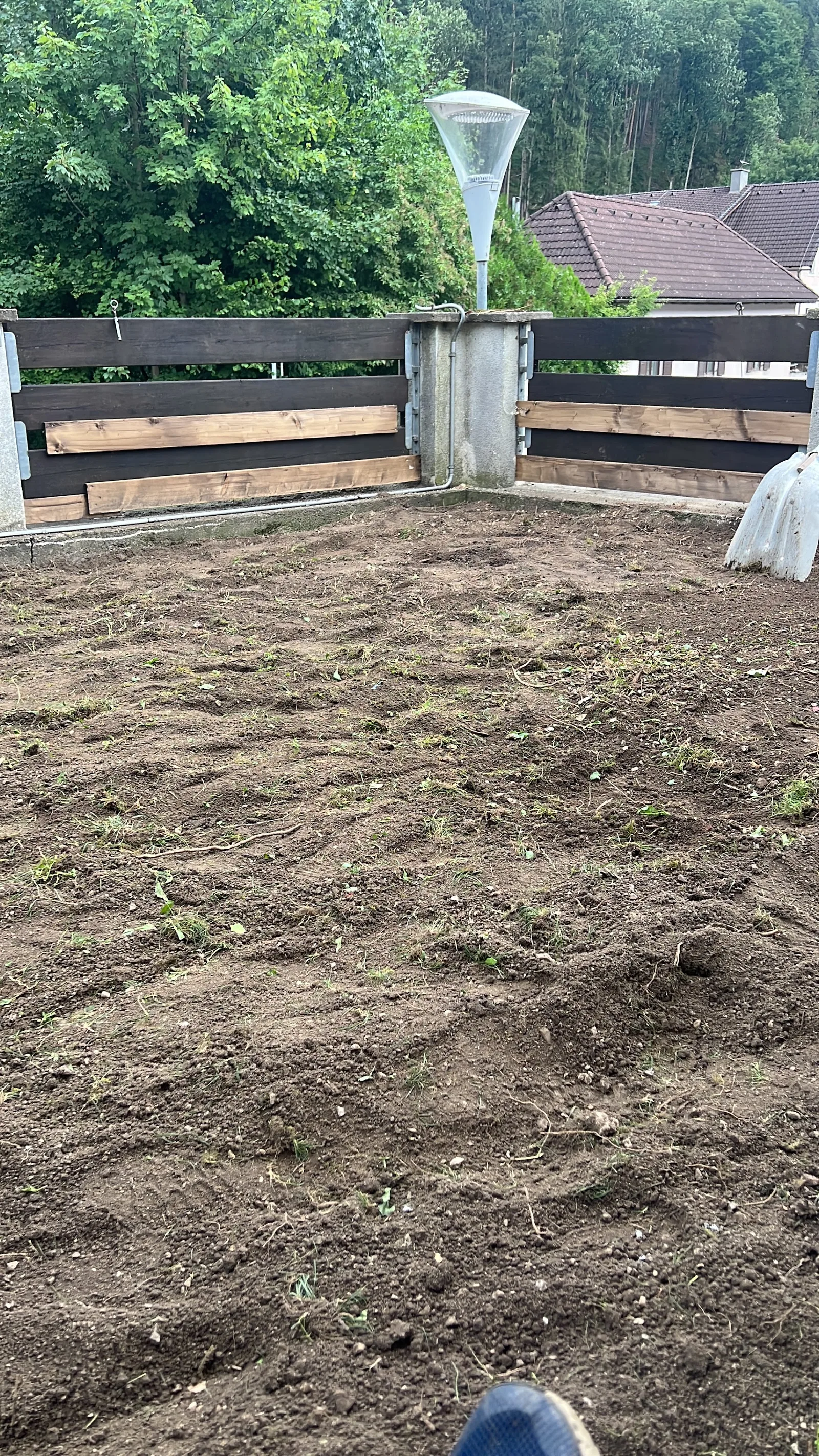 Umgegrabene Gartenfläche entlang eines dunklen Holzzauns